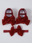 Baby girl in velvet-look red pram shoes with oversized bow, sitting on parent’s lap at christening