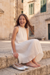 Rozalia white pleated dress for girls outdoors – sitting on stone steps