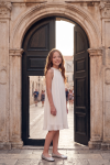 Rozalia white pleated dress for girls in front of a stone gateway – front view