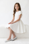Rumi white dress for girls – seated on a white bench, front view