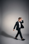 Sam black suit for boys with bow tie – boy in motion against a grey background, open blazer, full length